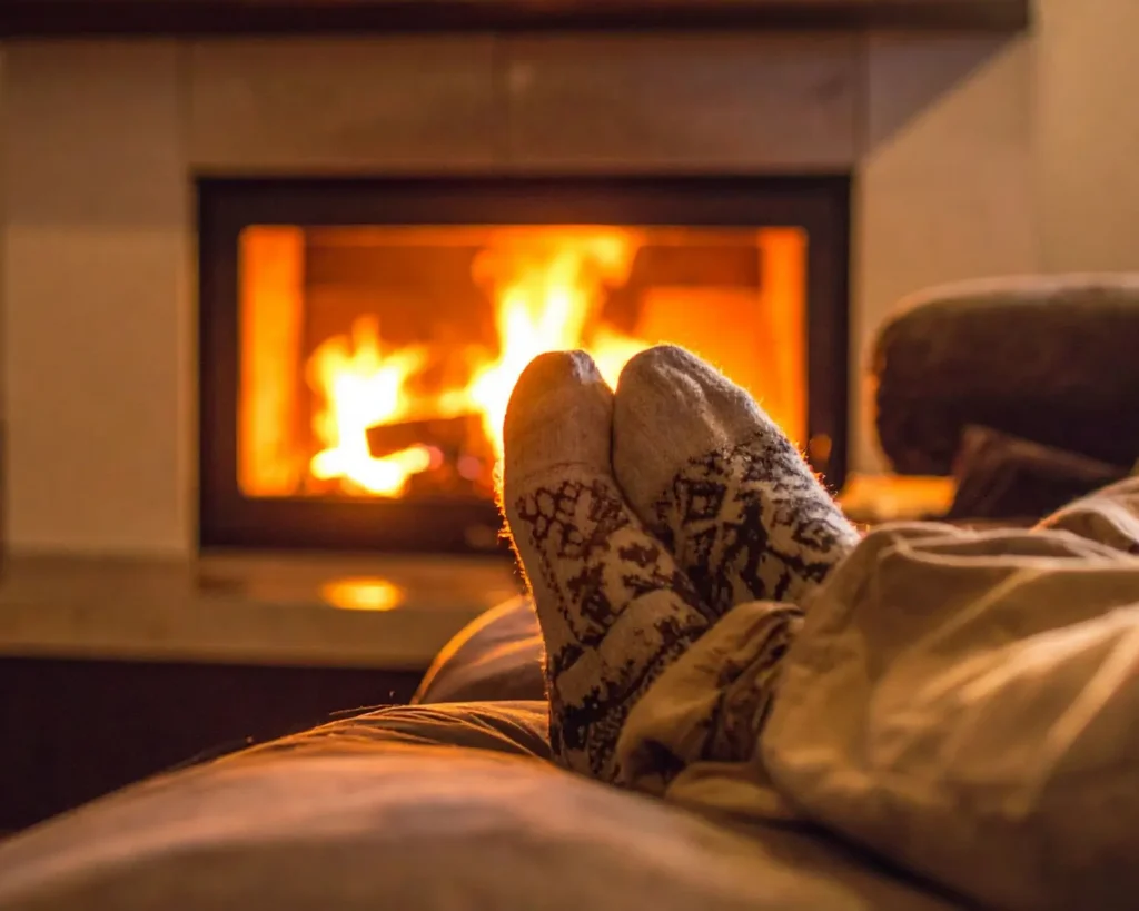 Person relaxing by a warm indoor fireplace in a cozy living room